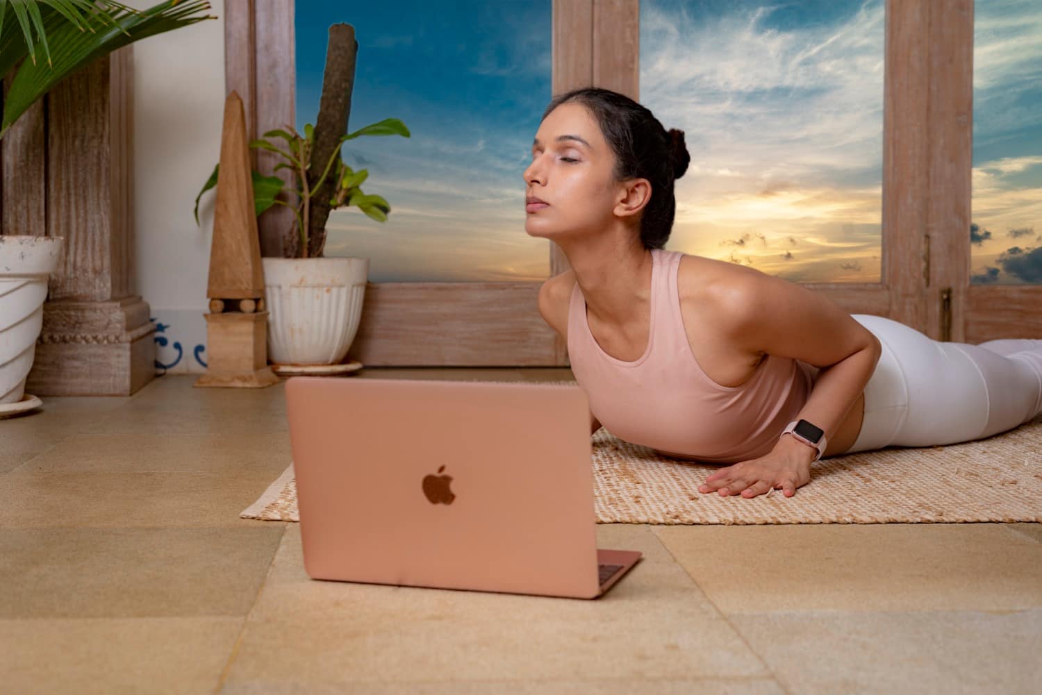 Ira Trivedi in a cobra pose on a mat at sunset, with a laptop open in front of her