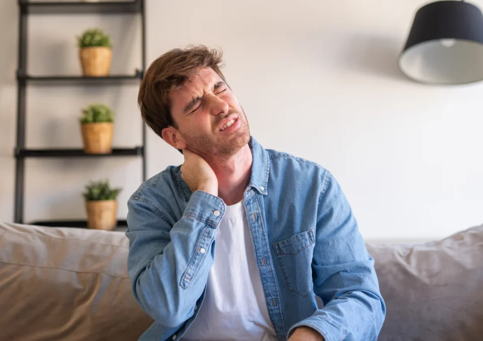 A man on a sofa rubs his stiff neck after a long day