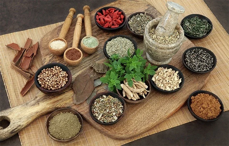 Bowls of dried herbs, roots and spices laid out beside a stone mortar